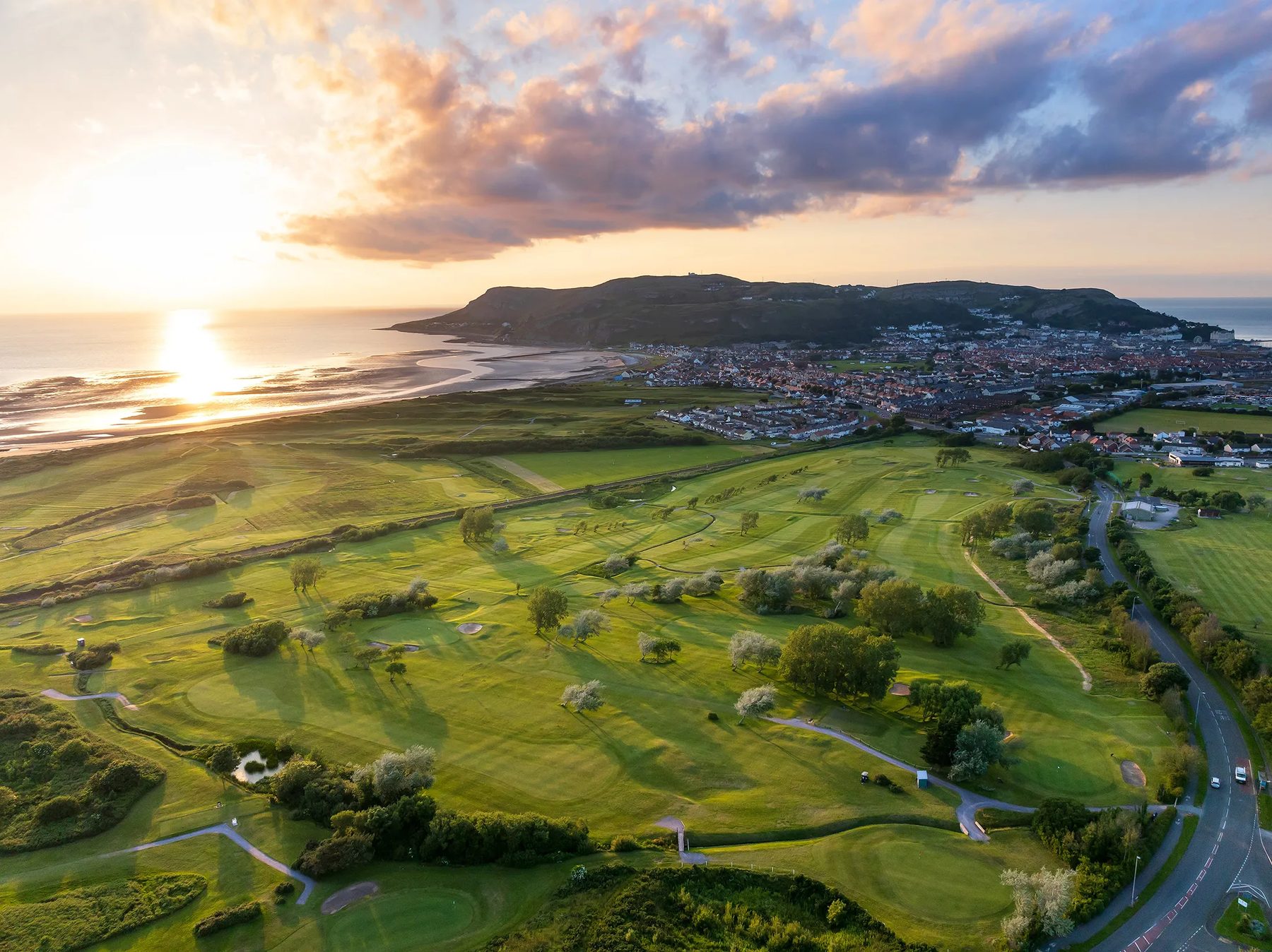 Aerial view at sunset over the course towards Llandudno, the Great Orme headland and the sea, with the low sun on the water